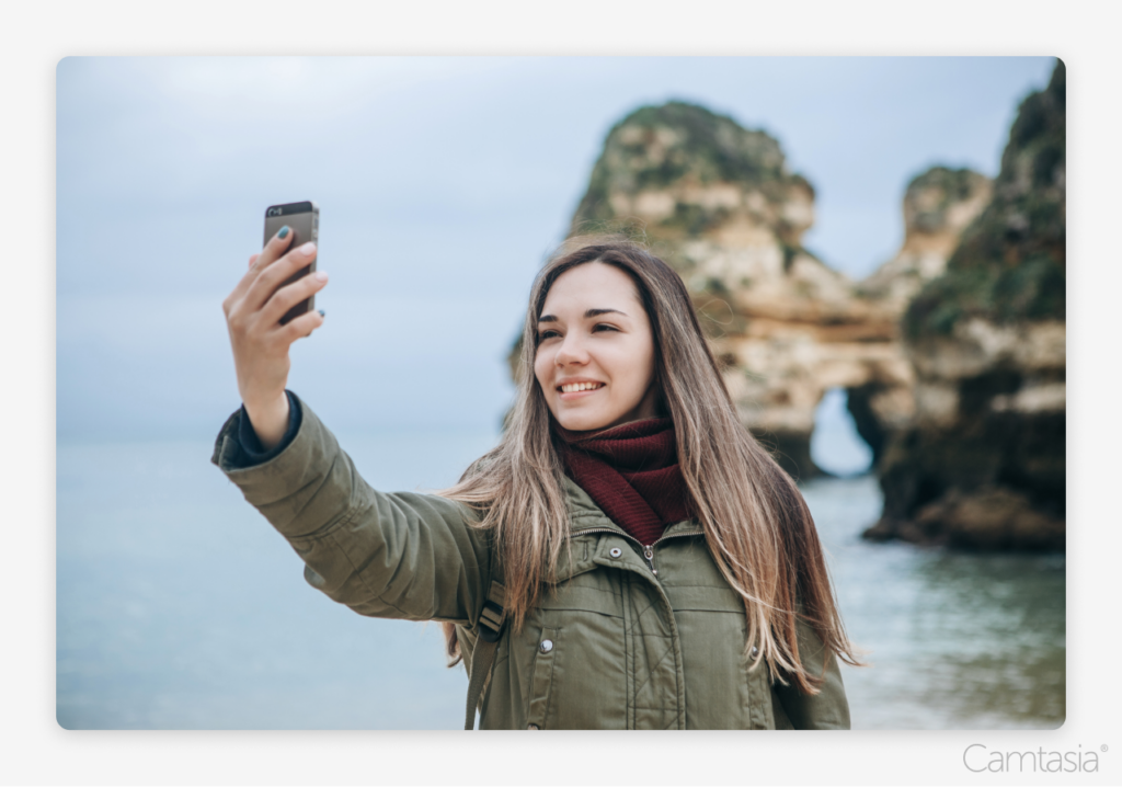 A picture of a woman taking a selfie in front of water and rocks.