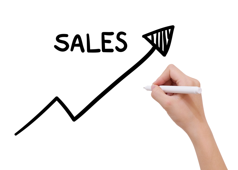 A hand with a pen drawing the word “Sales” and a rising arrow on the chart depicting sales growth