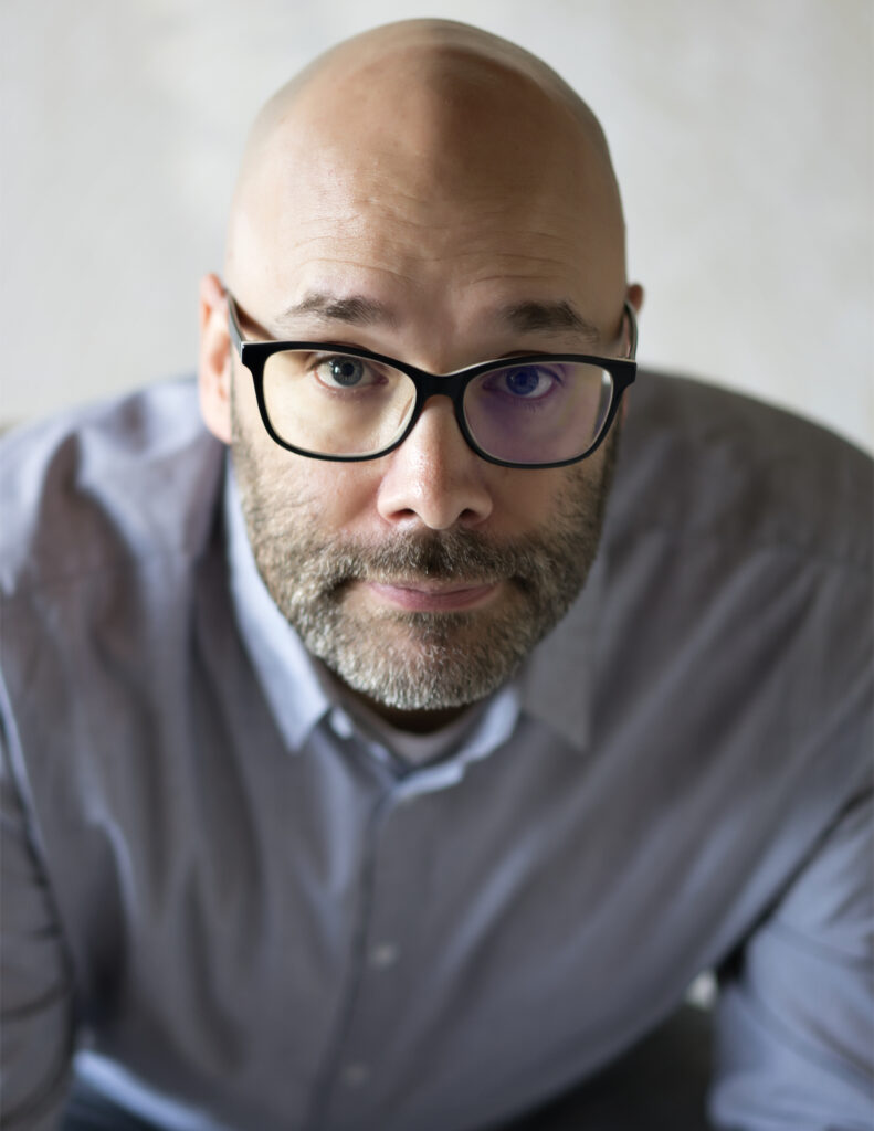 Person with glasses and a beard wearing a blue shirt looking at the camera.